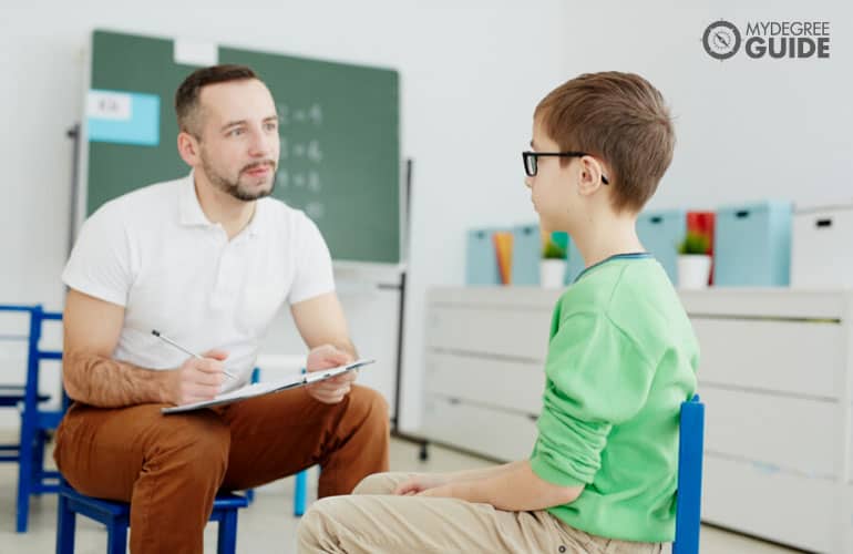 male psychologist talking to a young boy in a classroom