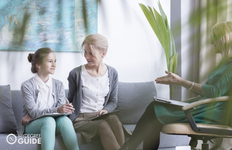 psychologist talking to a girl with her mother during therapy session