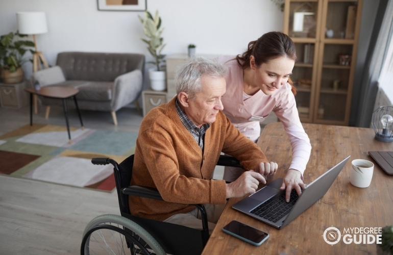 social worker helping an elderly man use a laptop